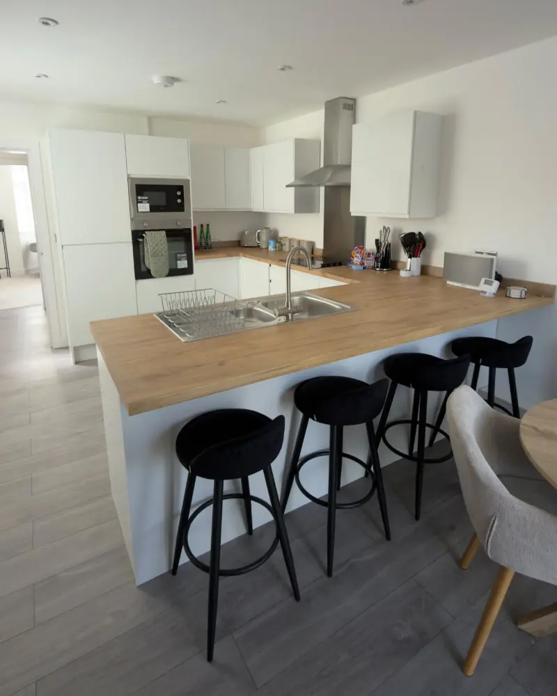 White kitchen with oak breakfast bar and black stools, cleaned by Blanc Cleaning